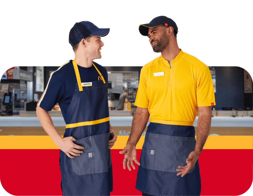 Two McDonald's employees wearing yellow and navy McDonald’s uniforms and aprons, standing together inside a restaurant.